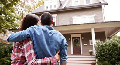 couple standing in front of and looking at their new house